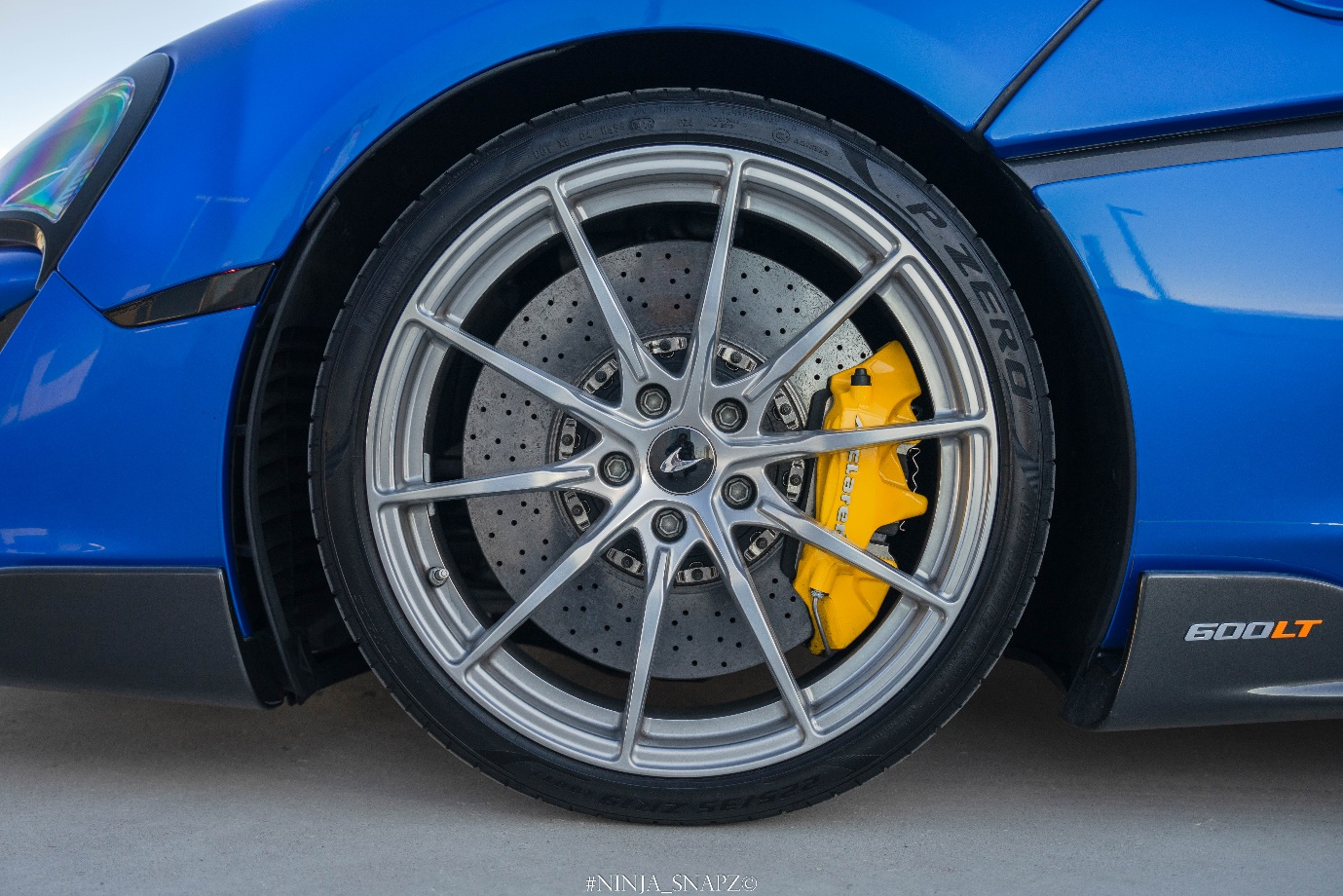 The McLaren 600LT Spider Blue is shown with a close-up of its wheel.