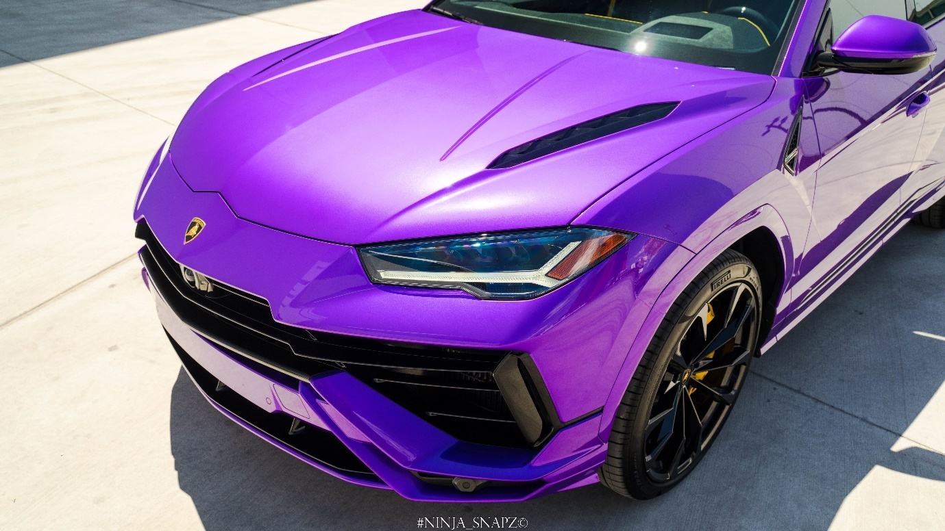 The Lamborghini Urus S in purple color is parked on a pavement.